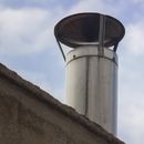 Close-up of a steel chimney pipe on a rooftop with a blue sky background, emphasizing industrial architecture.