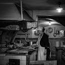 Black and white image of a chef working in a rustic kitchen, evoking a vintage ambiance.
